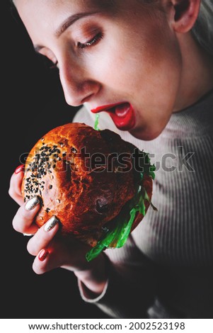 young woman eating burger in hands on black background