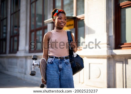 Portrait of happy african-american woman with skateboard. Young stylish woman with skateboard outdoors.	