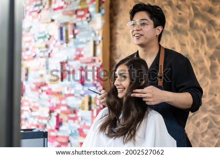 Asian hairstylist male combing and using scissors cut woman's hair. Professional Hairdresser or barber giving treatment and occupation service to smiling young beautiful girl customer in beauty salon. Royalty-Free Stock Photo #2002527062