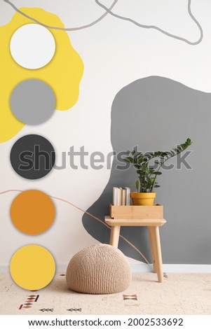Table with houseplant, books and ottoman near color wall in room. Different color patterns