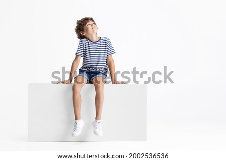 Looking up. Little Caucasian preschool boy sitting on box isolated over white studio background. Copyspace for ad. Happy childhood, education, emotions, facial expression concept. Having fun Royalty-Free Stock Photo #2002536536