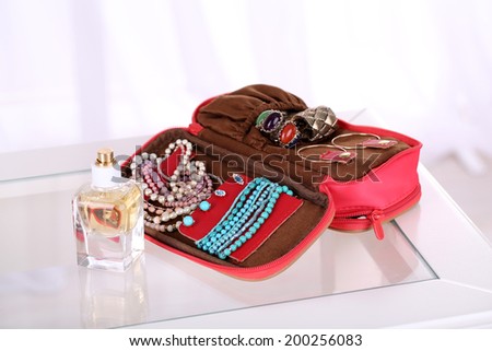 Handbag with accessorises and perfumes in bottles on table on  home interior background