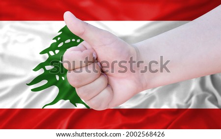 Hand makes a thumbs up sign on the background of the flag of Lebanon. like, good, positive