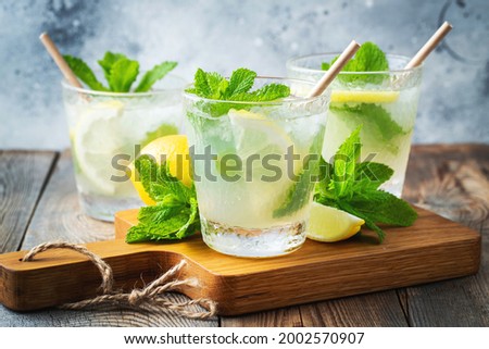 Two glass with lemonade or mojito cocktail with lemon and mint, cold refreshing drink or beverage with ice on rustic blue background. Royalty-Free Stock Photo #2002570907