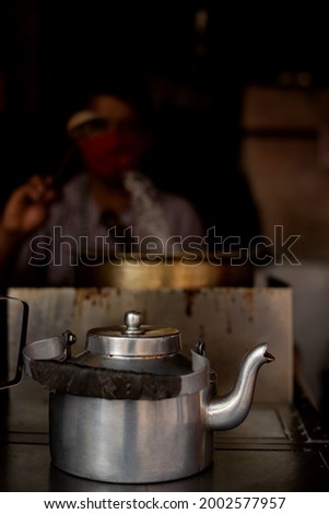Kettle of hot chai with blurred  picture of vendor making the same