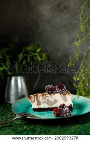 Cheesecake with chocolate flavor is on a plate with blackberries In the background a bank with mint 