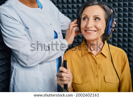 Portrait senior woman with white toothy smile while hearing check-up with ENT-doctor at soundproof audiometric booth using audiometry headphones and audiometer Royalty-Free Stock Photo #2002602161