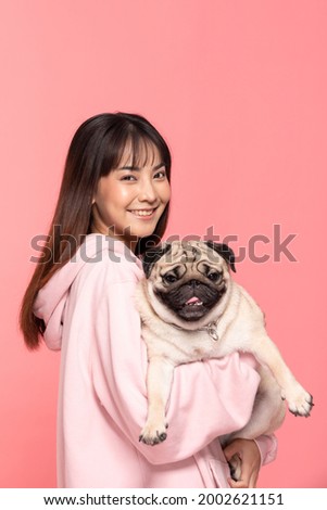 Beauty Asian young woman holding dog pug breed on her arm smile and happiness,Owner hug her cute pet dog with love on pink background,Young girl with adorable dog purebred pug breed looking on camera  Royalty-Free Stock Photo #2002621151