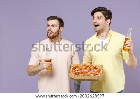 Two shocked amazed young men friends together wear t-shirt tattoo translate fun eat italian pizza in cardboard flatbox drink beer look aside isolated on purple background People lifestyle concept.