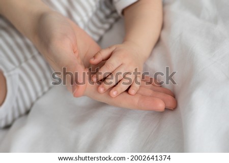 Mother Baby Connection. Mom And Little Newborn Baby Joined Hands Together, Closeup Shot Of Little Infant Child With Tiny Fingers Placed Arm On Mommy's Palm, Young Family Bonding At Home, Cropped