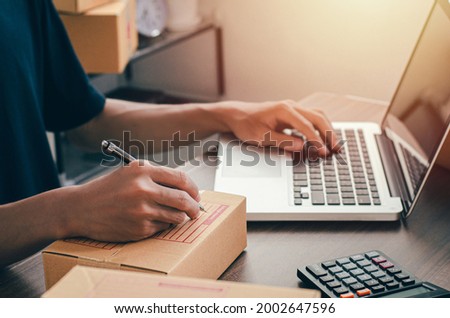 Young man sitting at home packing to be sent by post Ready to write the customer contact address from the notebook to send the destination.