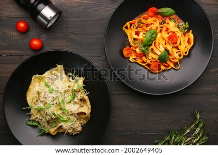 two plate with pasta top view. alfredo pasta with beef and marinara pasta on wooden table with ingredients, pepper and cheese. Royalty-Free Stock Photo #2002649405
