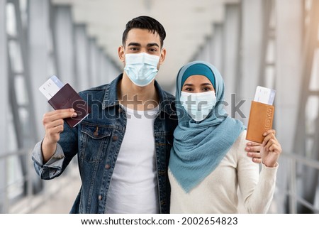 Portrait Of Muslim Couple In Medical Masks With Passports And Tickets In Airport, Positive Islamic Spouses Ready For Vacation Flight, Enjoying Safe Travels During Coronavirus Pandemic, Closeup Royalty-Free Stock Photo #2002654823
