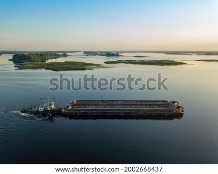 Barge on a wide river in the rays of sunrise. Aerial drone view.
