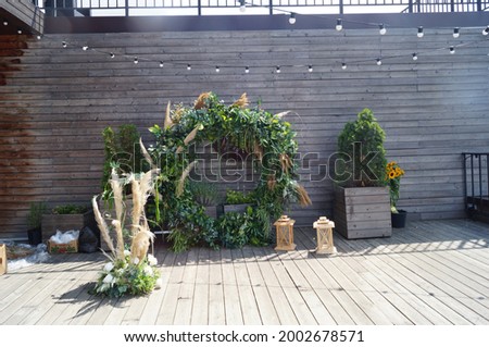 
exit wedding ceremony in eco style an arch in the form of a circle of green leaves and brown pampas grass on a background of wooden boards