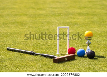 a set of colored balls, a hammer and a winners prize at the croquet hoop on the green lawn Royalty-Free Stock Photo #2002679882