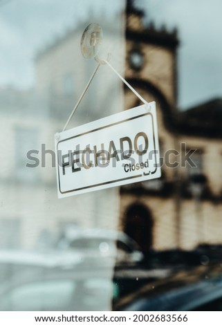 A sign board through the glass of store window written in portuguese: We are closed.