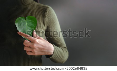Green Energy, ESG, Renewable and Sustainable Resources. Environmental and Ecology Care Concept. Close up of Hand Holding a Heart Shape Green Leaf on Chest Royalty-Free Stock Photo #2002684835
