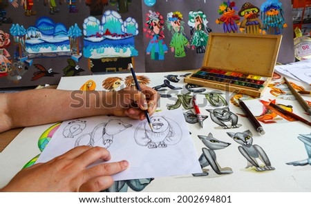 The animator draws with a pencil and draws characters from cartoons, comics or puppet shows. Preparing to make a doll. The designer creates sketches. Comics, cartoons, puppet theater Royalty-Free Stock Photo #2002694801