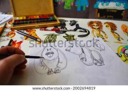 The animator draws with a pencil and draws characters from cartoons, comics or puppet shows. Preparing to make a doll. The designer creates sketches. Comics, cartoons, puppet theater Royalty-Free Stock Photo #2002694819
