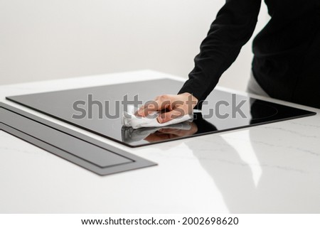 Woman polishing her ceramic induction cooktop built in kitchen appliances with tissue, using special cleaning chemicals to clean glossy white counter, cropped shot Royalty-Free Stock Photo #2002698620