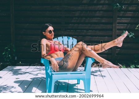 Beautiful tanned fit slender woman in bikini in backyard  posing on chair, summer vibes