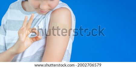 Teenage boy show to adhesive bandage plaster on his arm gesturing Okay after vaccination on blue background. Injection covid vaccine, healthcare for children.