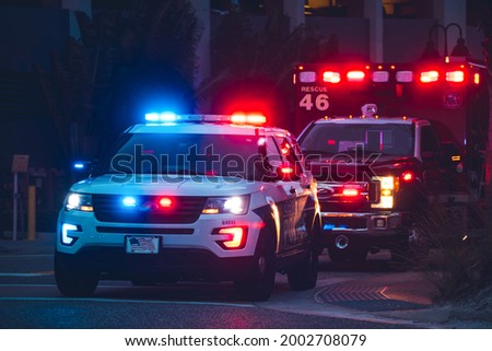 American Police Car and Emergency truck with Blue and red lights. US Paramedic Fire Rescue resuscitation help. Investigation Crime, murder, theft, police arrest. Photo has a dramatic toning. Royalty-Free Stock Photo #2002708079
