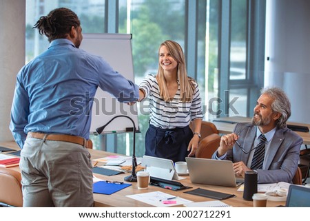 Young modern men in smart casual wear shaking hands and smiling while working in the creative office. Glad to work with you! Mature businessman shake hands with a younger colleague