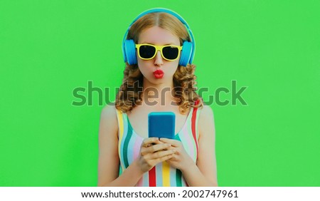 Summer colorful portrait of stylish young woman listening to music in headphones with smartphone on green background