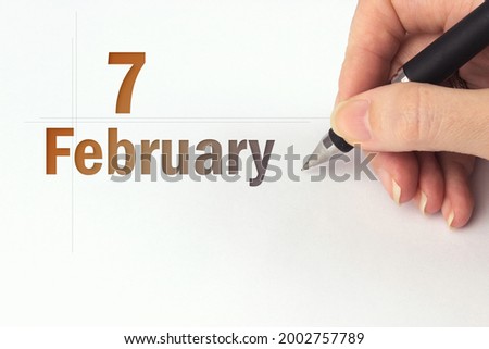 February 7th. Day 7 of month, Calendar date. The hand holds a black pen and writes the calendar date. Winter month, day of the year concept
