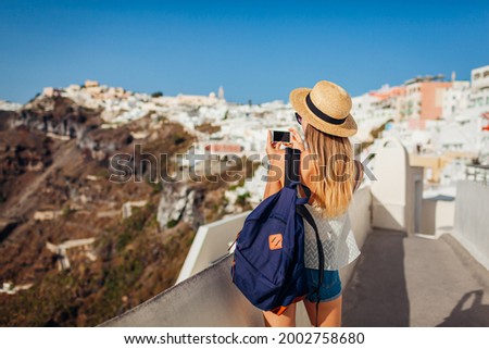 Santorini traveler woman taking photo of Thera, Fira traditional greek village architecture on smartphone. Tourism, traveling, summer vacation