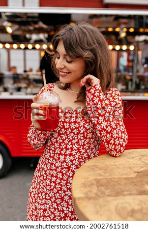 Romantic pretty girl in summer dress smiling with closed eyes and drinking lemonade outside on summer terrace