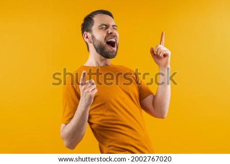 Attractive happy bearded football fan cheering for his favorite team celebrating victory. Lucky gambler placing bets at bookmakers website wining money. Isolated on yellow background.