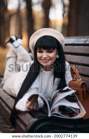 Picture of attractive woman lies on the old bench near the river and reads an intersting magazine