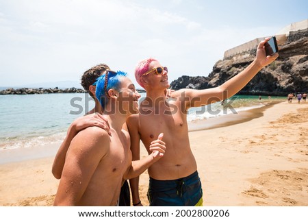 group of three happy and cheerful teenagers boys enjoying and smiling looking at the camera taking a selfie together at the beach.