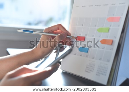 Event planner timetable agenda plan on schedule event. Business woman checking planner on mobile phone, taking note on calendar desk on office table. Calendar event plan, work planning Royalty-Free Stock Photo #2002803581