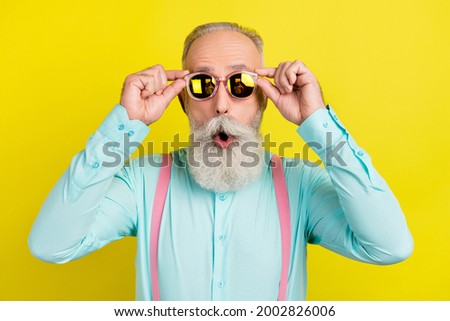 Photo portrait of bearded gentleman wearing turquoise shirt suspenders sunglass amazed surprised isolated yellow color background