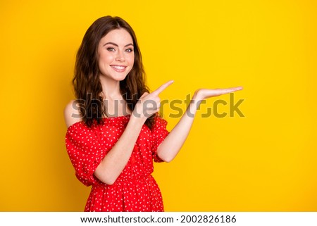 Photo portrait of happy girl in red dress pointing finger on palm keeping blank space isolated vibrant yellow color background