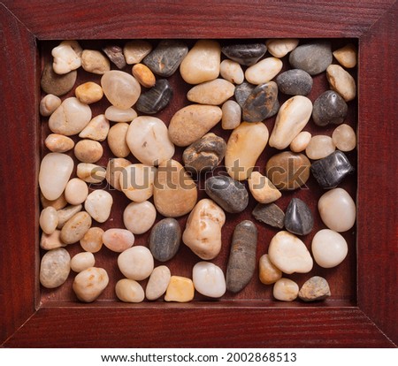 A wooden frame with sea pebbles, very close-up. Stones of two colors-light and dark. Empty space for text, inscriptions. Photo taken from above. A pleasant picture for the eyes.