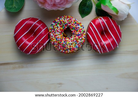 Three donuts of different colors lie on a wooden stand next to a rose. The concept of food, baking, sweets. Can be used as a background
