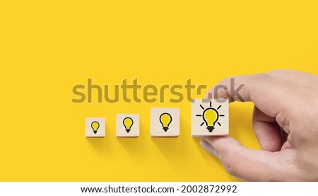 Concept creative idea and innovation. Hand picked wooden cube block with light bulb icon on yellow background Royalty-Free Stock Photo #2002872992