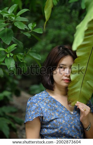 Short-haired Asian woman posing holding a leaf covering her face to take a photo.