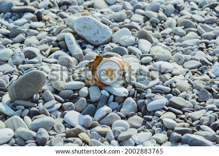 crumpled aluminum metal orange can on pebble beach, environmental protection concept, horizontal lifestyle stock photo image background