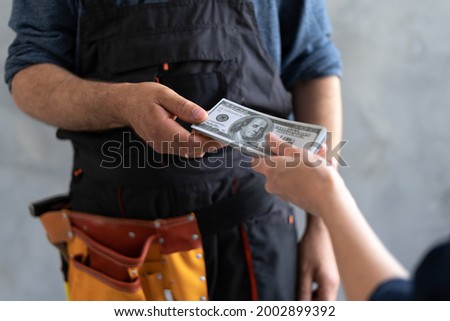 close-up female hand pays for the work of foreman builder repairman with dollar money. construction site concept. Focus on hands with money. business woman master deal. Royalty-Free Stock Photo #2002899392