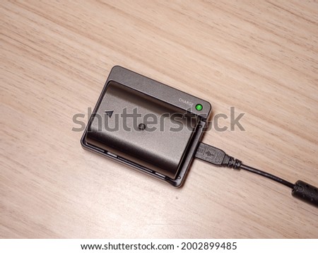 Camera charger and a battery being charged on a wooden desktop