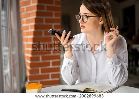business lady sitting in a cafe dictates a message audio voice recognition on a smartphone, virtual voice assistant. Turn on the microphone of the phone recording.Concept of gadgets and technology use