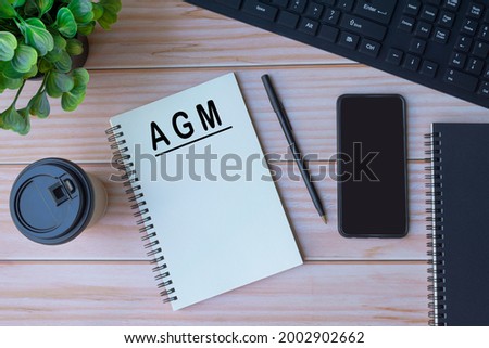 AGM on notepad with keyboard, pen, coffee and smartphone on wooden table Royalty-Free Stock Photo #2002902662