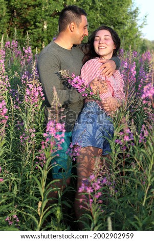 A beautiful young couple in love in a romantic photo session outdoors in a meadow with blooming pink flowers of fireweed.