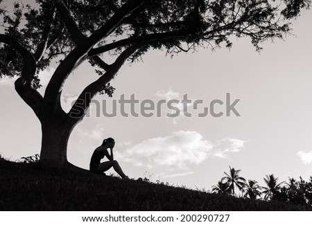 Silhouette of sad woman sitting under the tree.